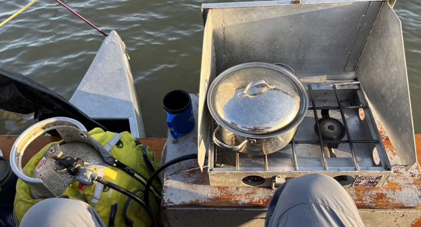 A cooking setup is arranged at the front of a canoe that is floating on water. 
